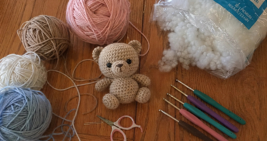 Matériel crochet avec peluche ours faite main, pelotes pastel, crochets, ciseaux et rembourrage sur table en bois