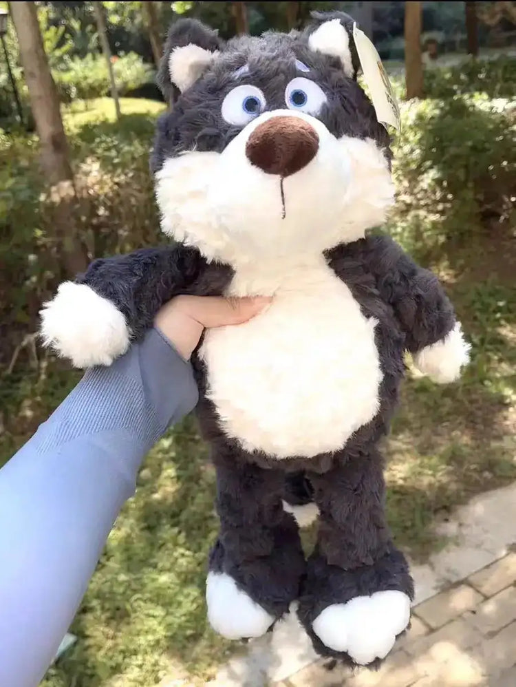 Peluche Loupio le loup tenu à la main en extérieur, montrant sa taille réelle, fourrure grise foncée et ventre blanc, yeux bleus ronds.